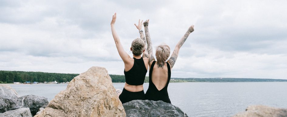 women sitting on rock while raising their hands